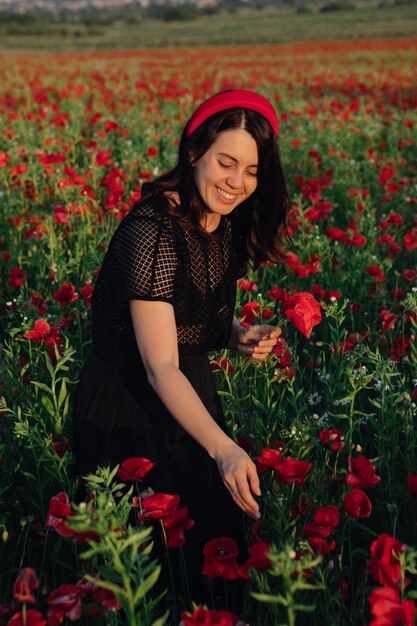 Hermosa mujer vestida de negro al atardecer en el campo de flores de amapola