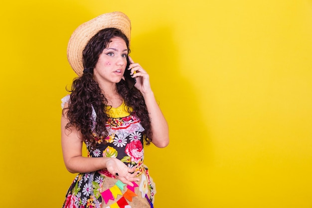 Hermosa mujer vestida con ropa típica para una Festa Junina hablando por llamada de audio en el teléfono celular