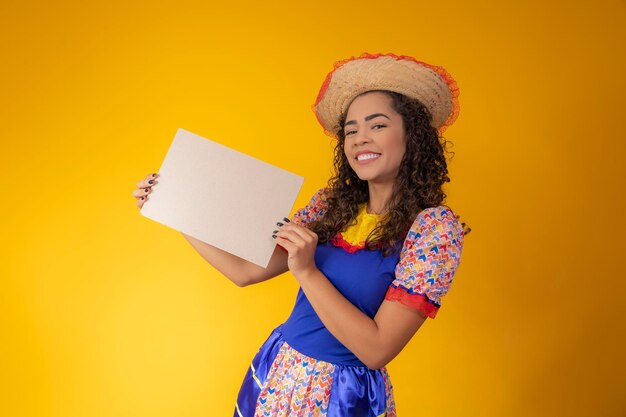 Hermosa mujer vestida con traje de festa junina sosteniendo un cartel en blanco con espacio de copia