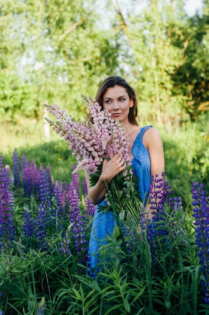 Hermosa mujer vestida con un vestido de flores lupines al atardecer