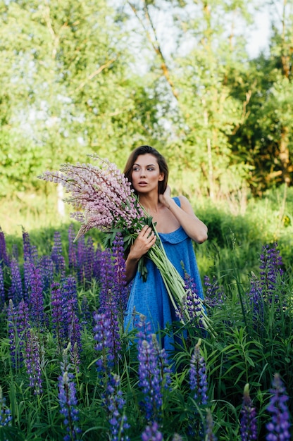 Hermosa mujer vestida con un vestido de flores lupines al atardecer