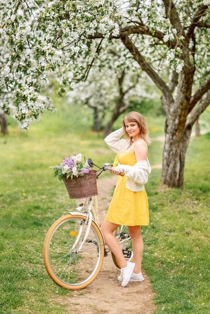 Foto una hermosa mujer con un vestido amarillo y una bicicleta camina por un jardín en flor en primavera.