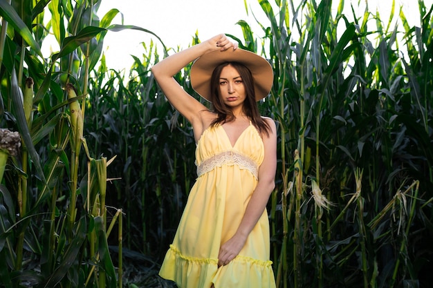 Hermosa mujer en vestido amarillo y sombrero posando en un campo de maíz