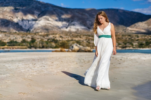 Una hermosa mujer con un vestido blanco caminando por la playa de elafonisi