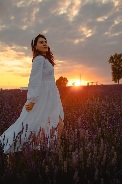 Hermosa mujer en vestido blanco en el campo de lavanda al atardecer