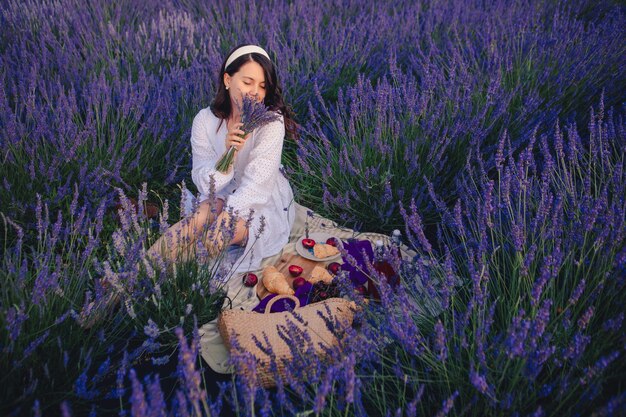 Hermosa mujer con vestido blanco en el campo de lavanda con picnic