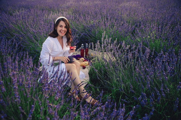 Hermosa mujer con vestido blanco en el campo de lavanda con picnic