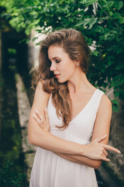 Hermosa mujer en vestido blanco contra las hojas del árbol verde