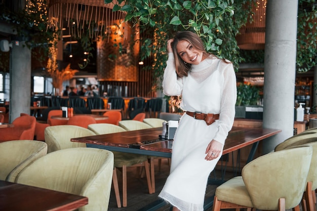 Hermosa mujer con vestido blanco de pie en el interior del restaurante