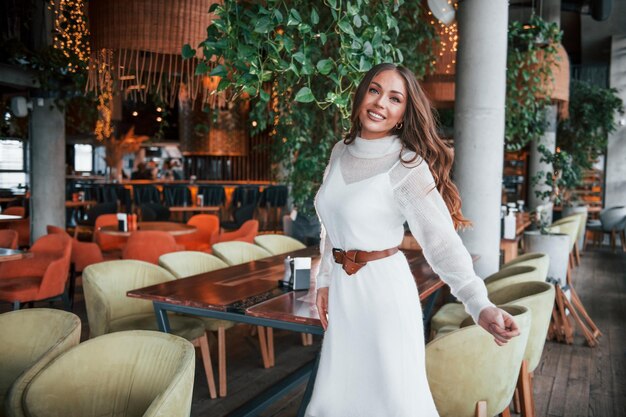 Hermosa mujer con vestido blanco de pie en el interior del restaurante