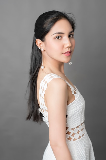 Hermosa mujer en vestido blanco retrato en estudio, fondo gris