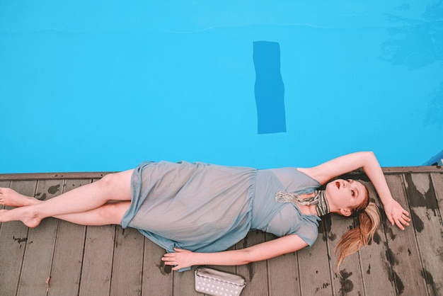 hermosa mujer en vestido de cóctel gris tendido cerca de la piscina