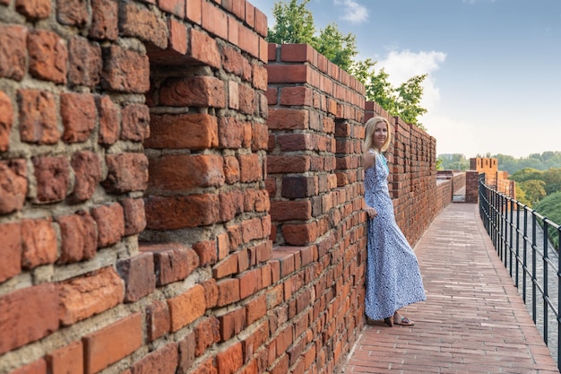 Hermosa mujer en un vestido se encuentra en la antigua pared de ladrillo rojo del castillo