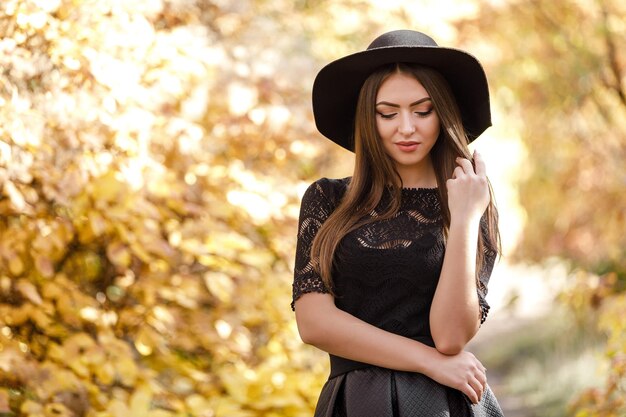 Hermosa mujer con vestido negro y sombrero en otoño