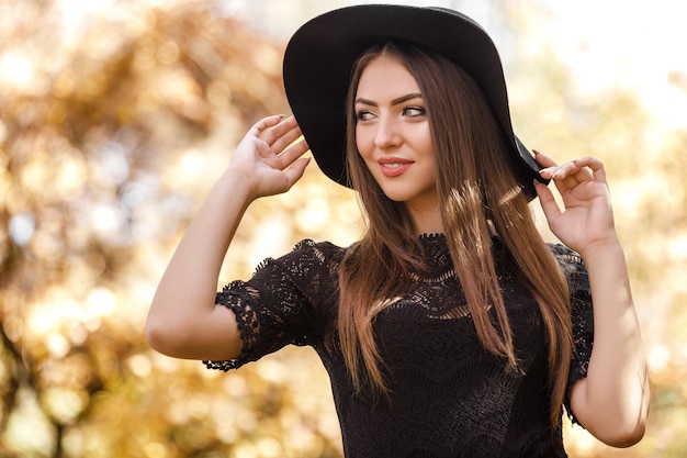 Hermosa mujer con vestido negro y sombrero en otoño