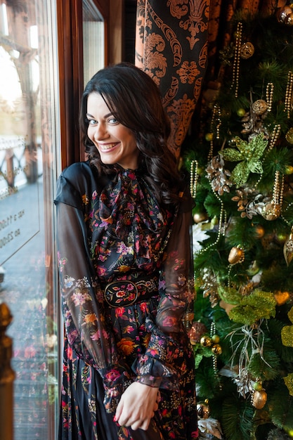 Foto hermosa mujer en vestido de noche cerca del árbol de navidad