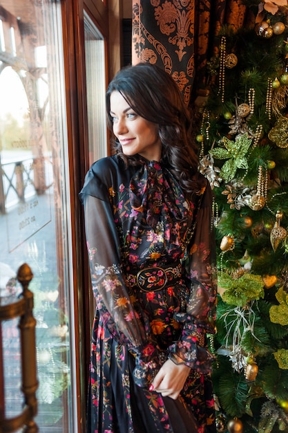 Hermosa mujer en vestido de noche cerca del árbol de Navidad