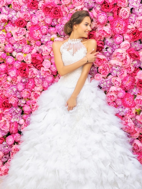 Hermosa mujer en un vestido de novia en una pared floral