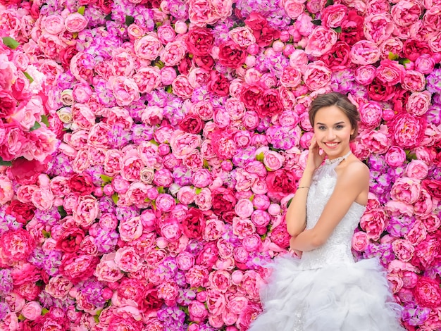 Hermosa mujer en un vestido de novia en una pared floral