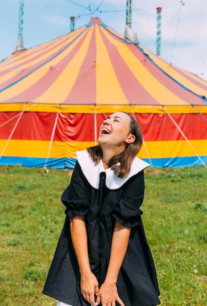 Hermosa mujer en vestido posa contra el telón de fondo de la carpa de circo en un día soleado