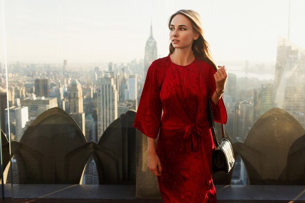 Hermosa mujer en vestido rojo y botas de cuero camina en el techo del Rockafeller Center en Nueva York