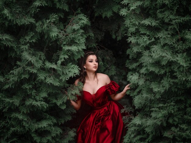 Hermosa mujer con vestido rojo caminando en el jardín lleno de rosas