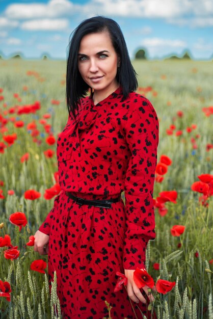 Hermosa mujer con un vestido rojo en un campo de flores de amapola