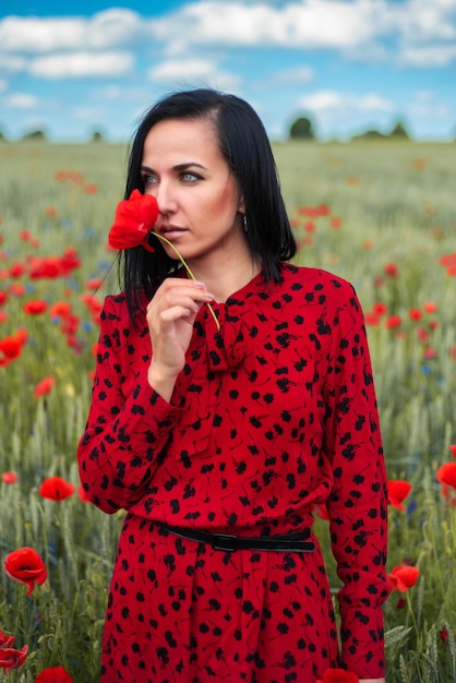 Hermosa mujer con un vestido rojo en un campo de flores de amapola