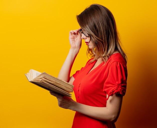 Hermosa mujer en vestido rojo con libro en pared amarilla