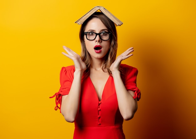 Hermosa mujer en vestido rojo con libro en pared amarilla