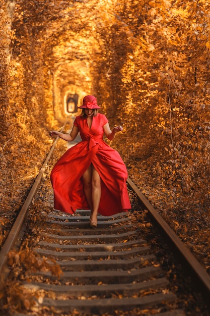 Hermosa mujer con vestido rojo de otoño camina por el túnel del amor