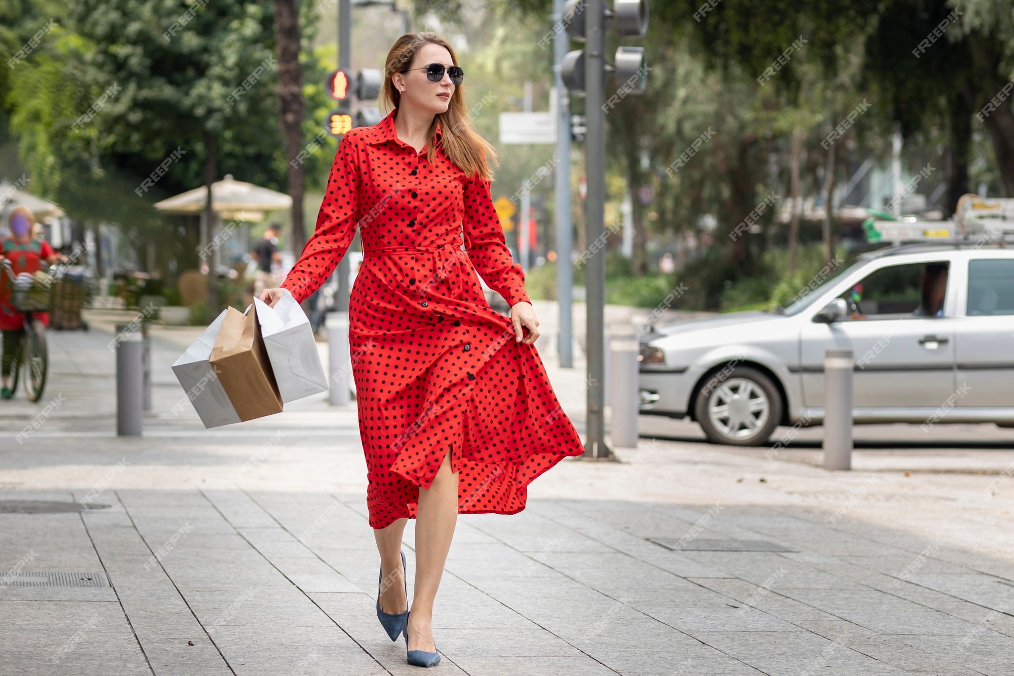 Hermosa mujer en vestido rojo verano caminando alegremente sonriendo por la calle mientras hace compras llevando sus bolsas. | Foto Premium