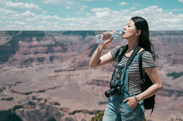 Hermosa mujer viajera bebiendo agua después de caminar hasta la cima del verano del parque nacional del gran cañón. señorita relajándose en el horizonte en un día soleado. chica asiática amor vida salvaje libertad de viaje.
