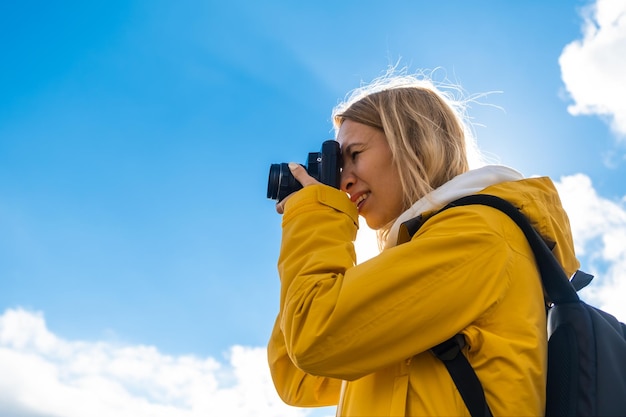 Hermosa mujer viajera con mochila toma fotos de la cámara contra el cielo azul con nubes