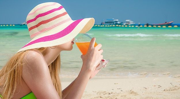 Hermosa mujer vistiendo bikini y sombrero beber jugo de naranja dormir en la playa