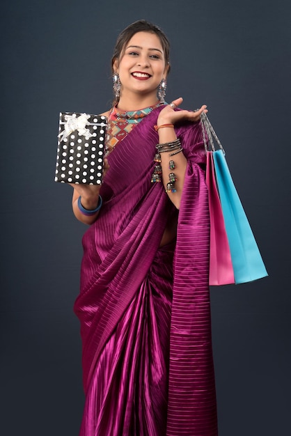 Hermosa mujer vistiendo un sari sosteniendo bolsas de compras y caja de regalo sobre un fondo gris