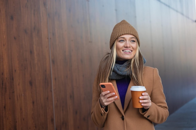 Hermosa mujer yendo a trabajar con café caminando cerca del edificio de oficinas Retrato de mujer de negocios exitosa sosteniendo una taza de bebida caliente