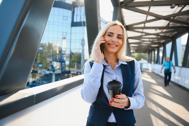 Hermosa mujer yendo a trabajar con café caminando cerca del edificio de oficinas Retrato de mujer de negocios exitosa sosteniendo una taza de bebida caliente