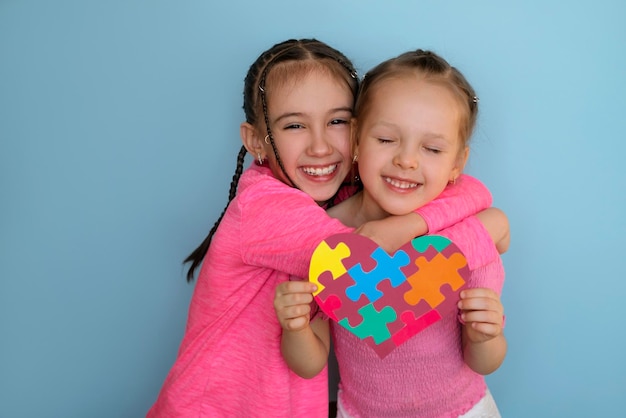 Hermosa niña abraza a su hermana con síndrome de autismo sosteniendo una tarjeta en forma de corazón