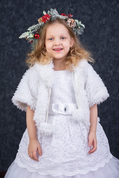 Hermosa niña con un abrigo de piel blanco con una corona de Navidad