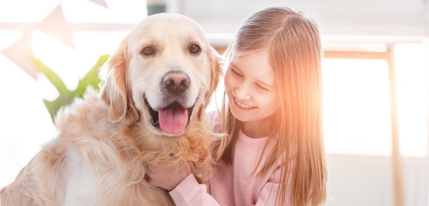 Hermosa niña acariciando adorable perro golden retriever en la habitación soleada en casa