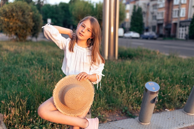 Hermosa niña al atardecer con un sombrero de paja se alisa el pelo