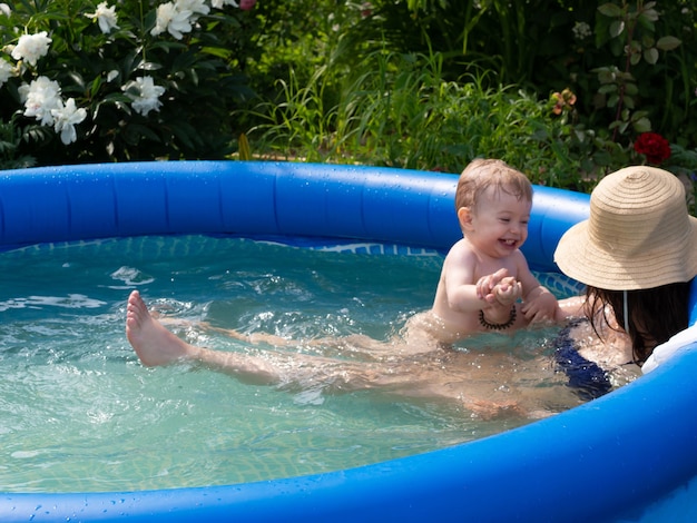 Hermosa niña de un año se baña y juega en una piscina inflable con mamá en un día caluroso