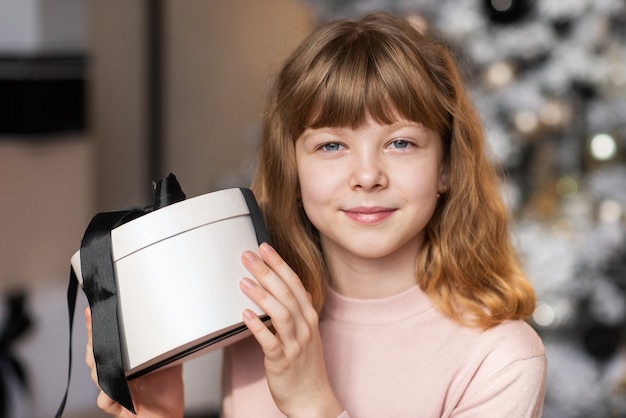 Hermosa niña de año nuevo sosteniendo un regalo y mirando a la cámara