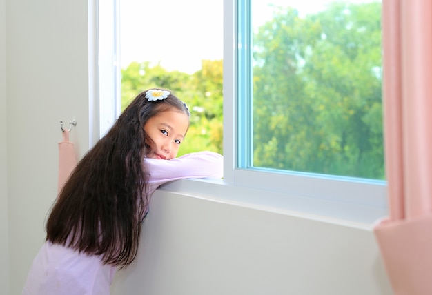 Hermosa niña asiática niño en casa acostado en la ventana de la casa