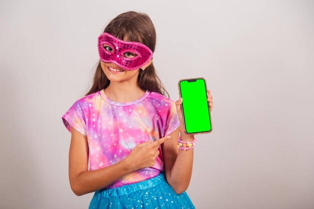 Hermosa niña brasileña vestida para el carnaval en Brasil mostrando smartphone con pantalla Chroma verde