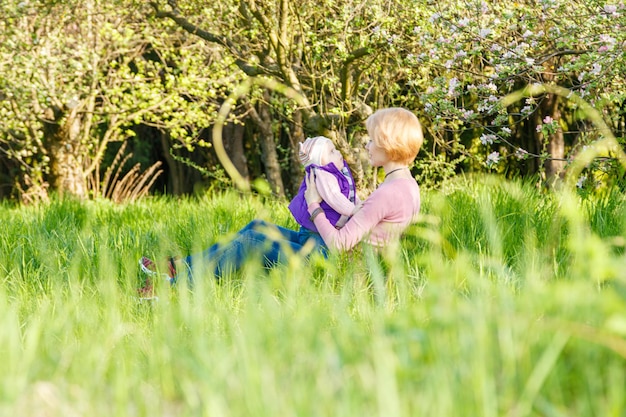 Una hermosa niña en los brazos de una niña en un parque en flor en primer plano