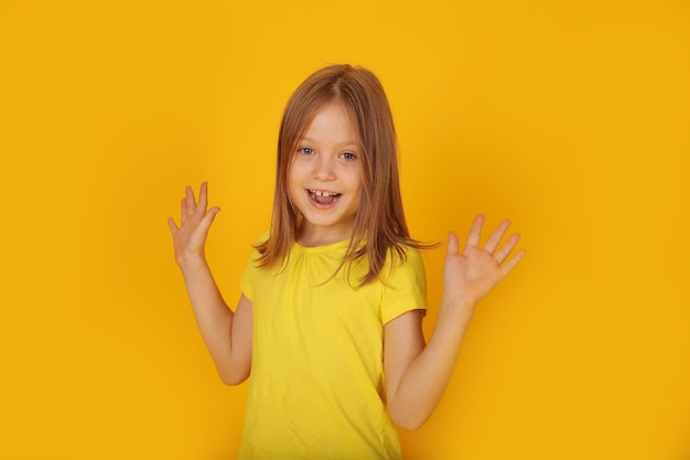 Una hermosa niña de cabello castaño con una camiseta amarilla se sorprende con un fondo amarillo.