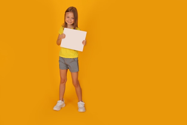 una hermosa niña de cabello castaño con una camiseta amarilla sostiene una hoja de papel blanca