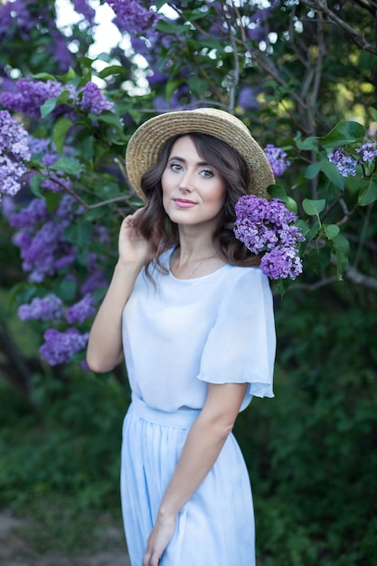 Hermosa niña con cabello castaño ondulado en un sombrero de paja en un jardín lila en flor vacaciones de verano